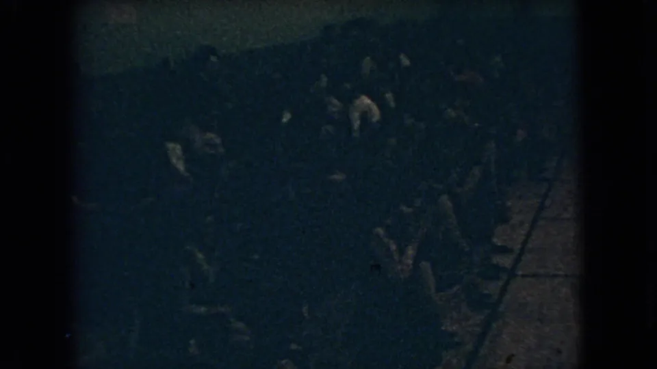 1966 Ohio 8mm frame with a dark, grainy view of people standing close together during an indoor celebration, with individual faces not clearly readable.