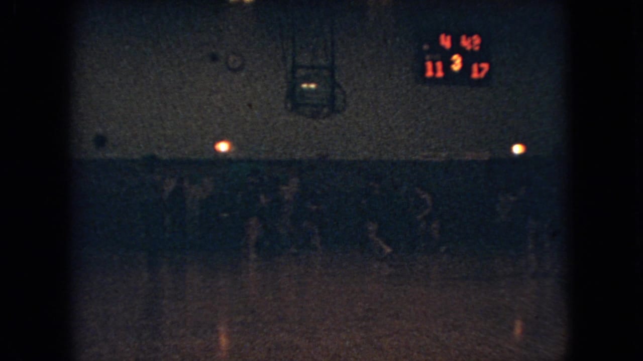 Dim 1966 Ohio school basketball game frame with players moving across a gym floor under a scoreboard showing 11-17 and 4:48 remaining.