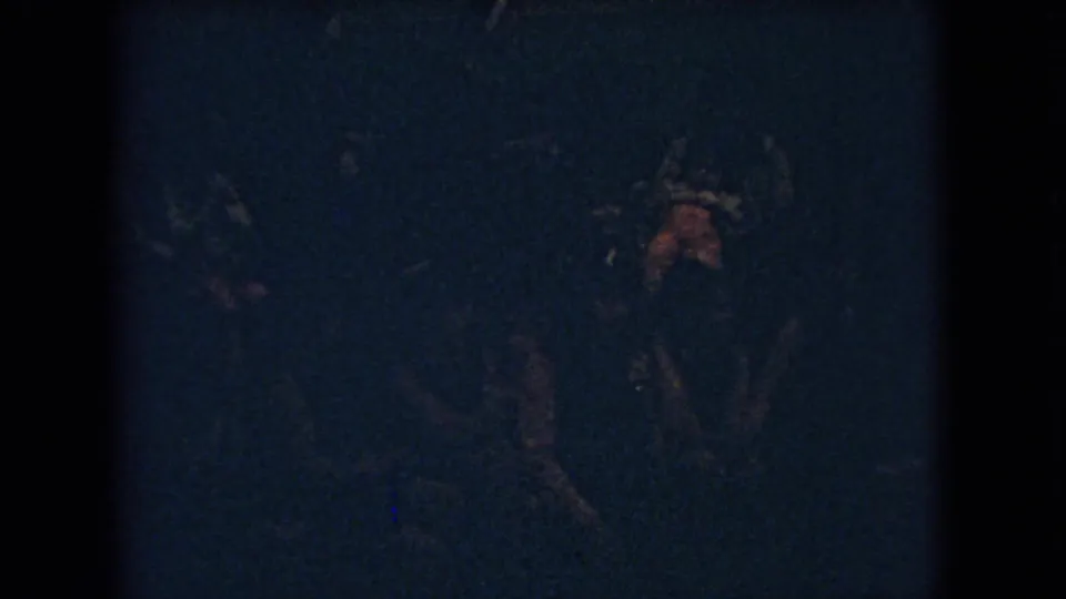 Underexposed 8mm frame from the Ohio school basketball clip, with a blurred player figure visible near the right edge of the gym scene.