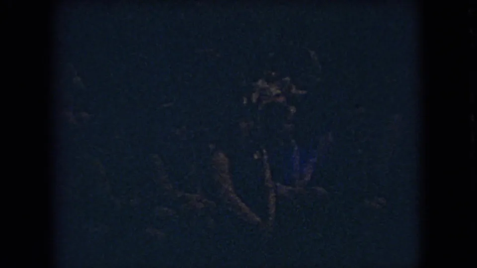 Low-light 1966 Ohio basketball frame showing indistinct players in dark uniforms moving across a shadowed school gym court.