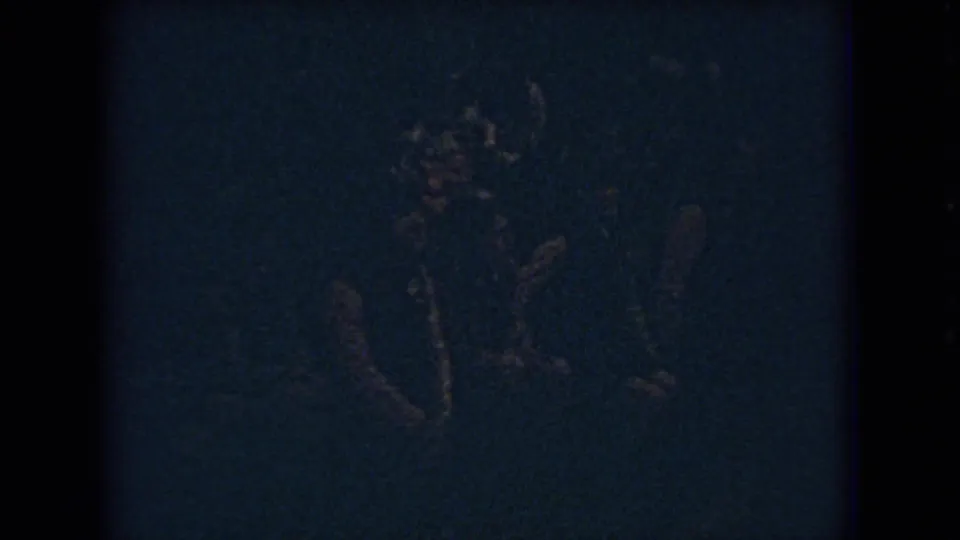 Grainy 8mm frame from a 1966 Ohio school basketball game, showing blurred players clustered on a dim gym court with one figure low near the floor.