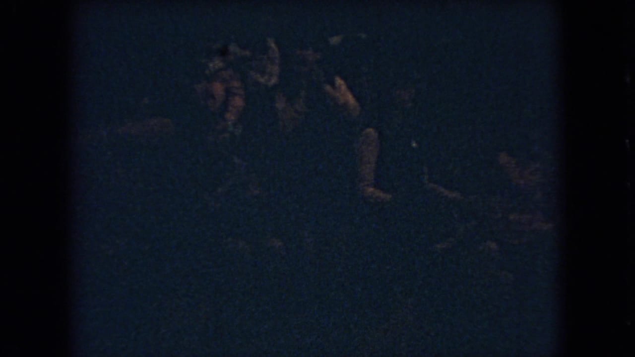 In metadata-supported 1966 Ohio footage, shadowed spectators stand near a dimly lit basketball game with only faces and hands faintly visible.