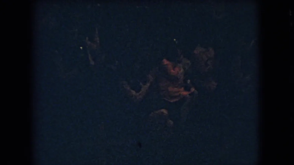 A dark 8mm frame shows several indistinct people near the basketball play area, with reddish artificial-light highlights catching faces or hands.