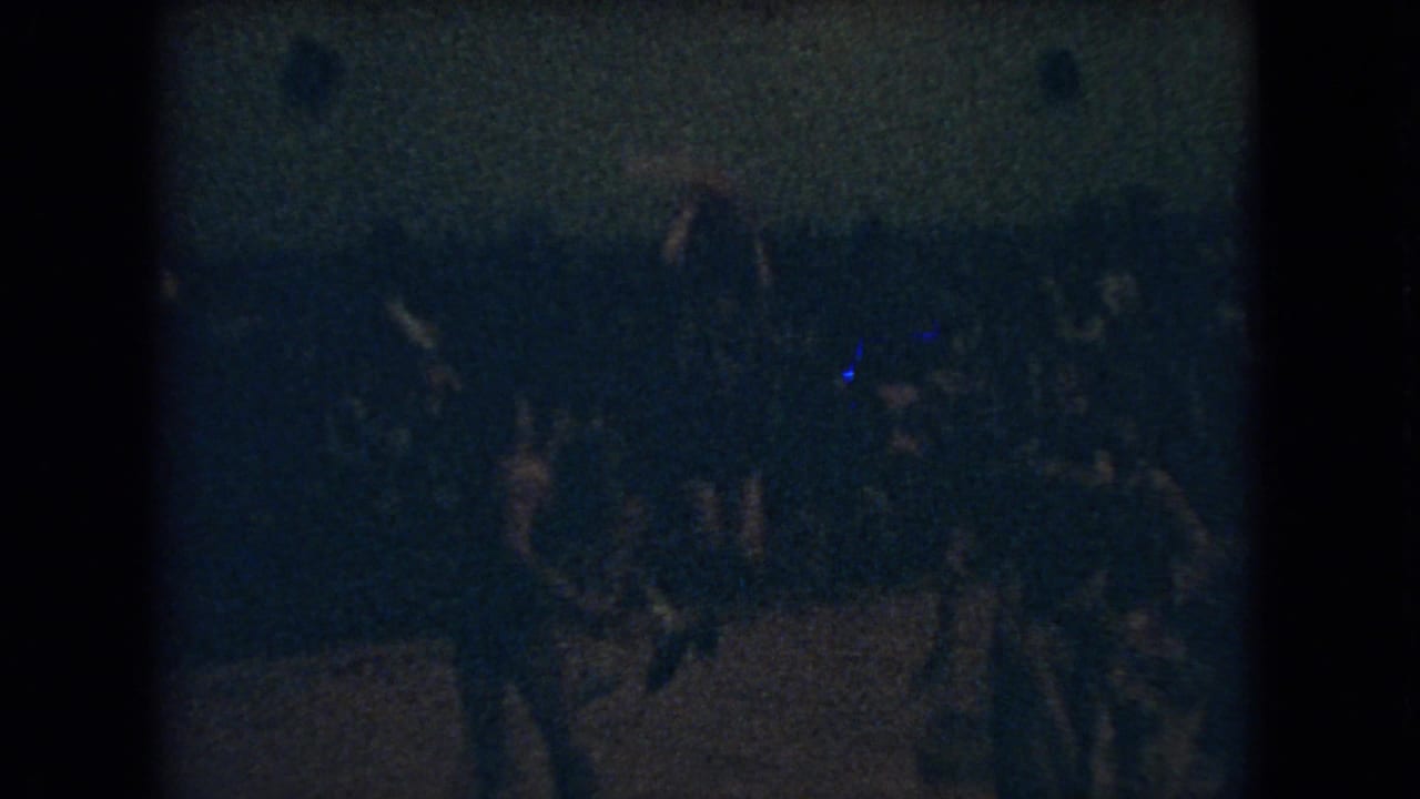 Grainy 1966 Ohio 8mm frame showing a dimly lit indoor basketball game with players crossing a wooden court and spectators in the background.