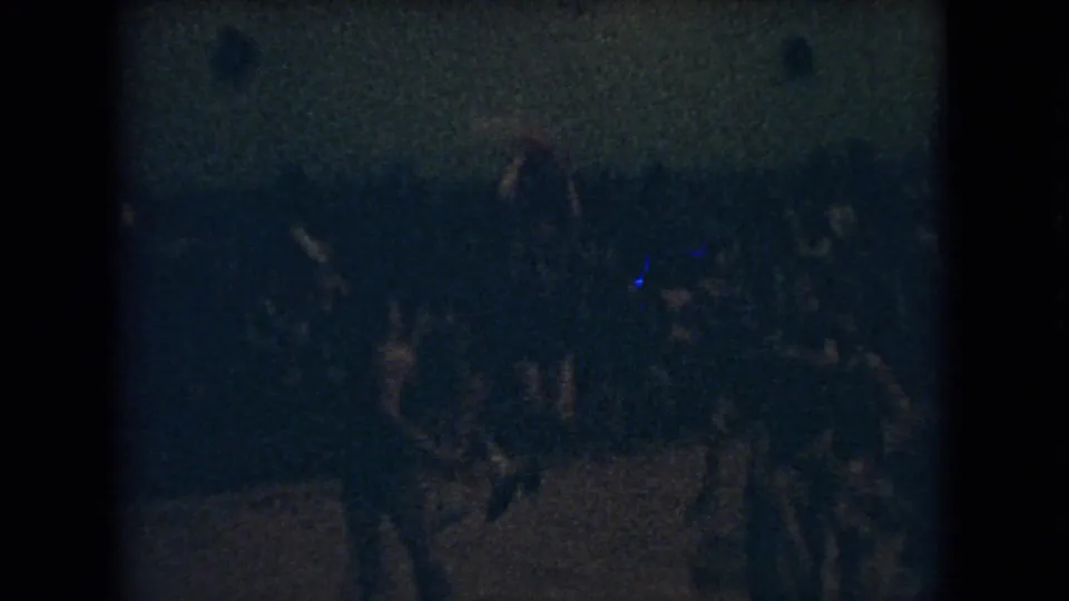 Grainy 1966 Ohio 8mm frame showing a dimly lit indoor basketball game with players crossing a wooden court and spectators in the background.