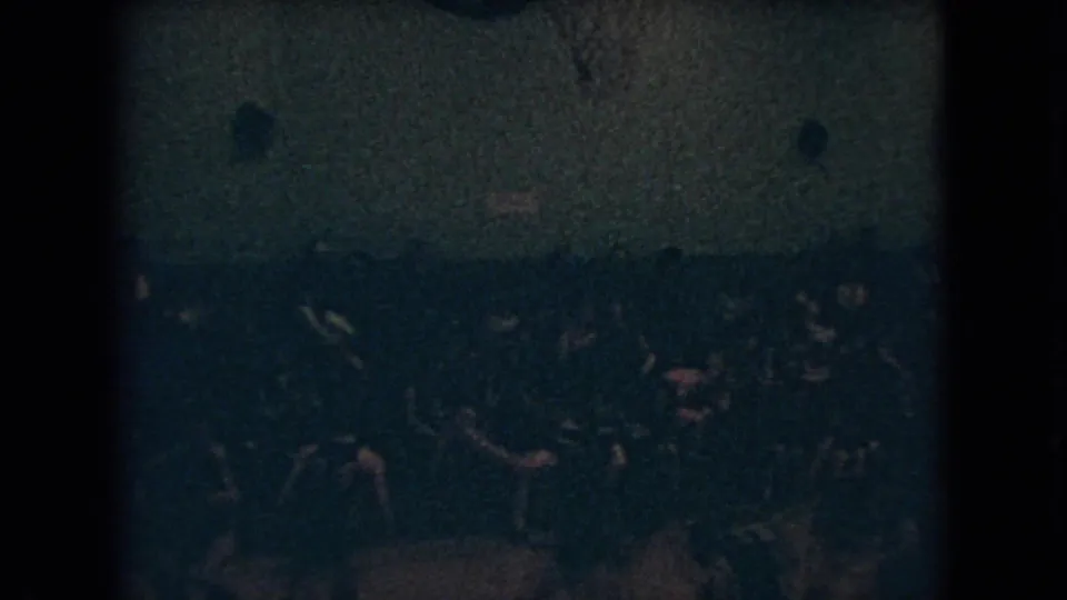 Low-light 8mm frame from an Ohio basketball game in 1966, with several players gathered near the far side of the court and a seated crowd behind them.