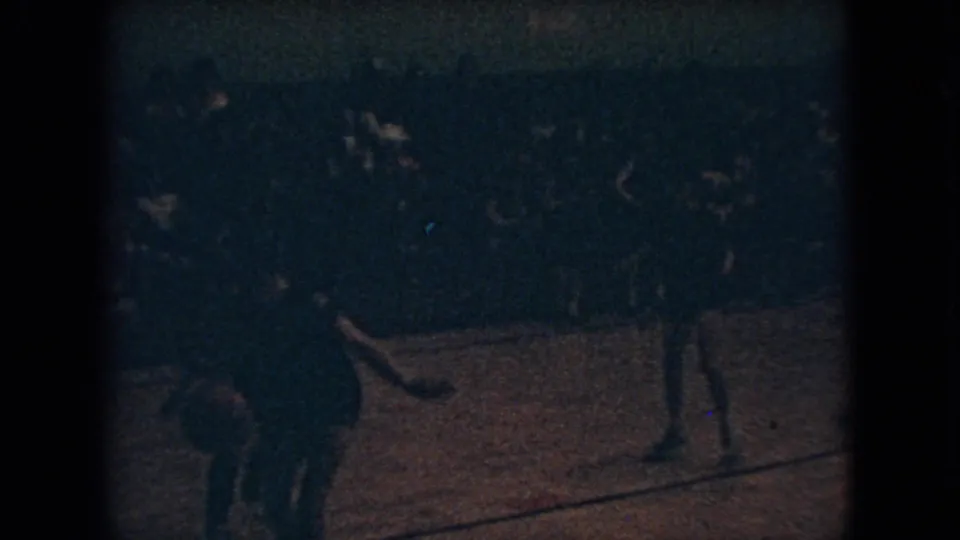 Dim 1966 Ohio home-movie frame showing a basketball player on the wooden court with other players and spectators softened by grain and low exposure.