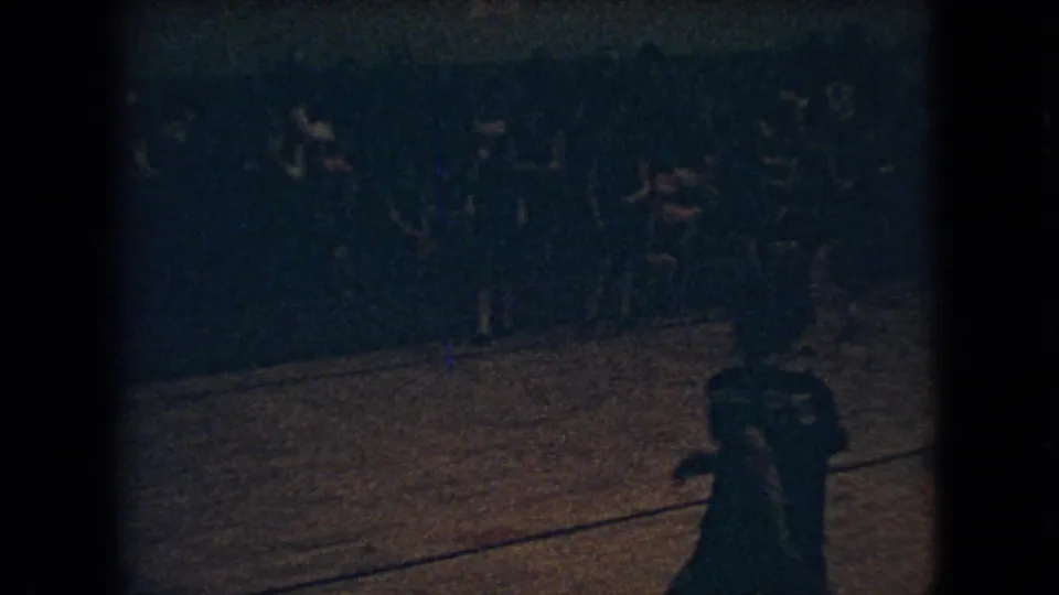 Final low-light 8mm frame of the 1966 Ohio indoor basketball game, with a moving foreground player, distant players, and spectators lining the far side of the gym.
