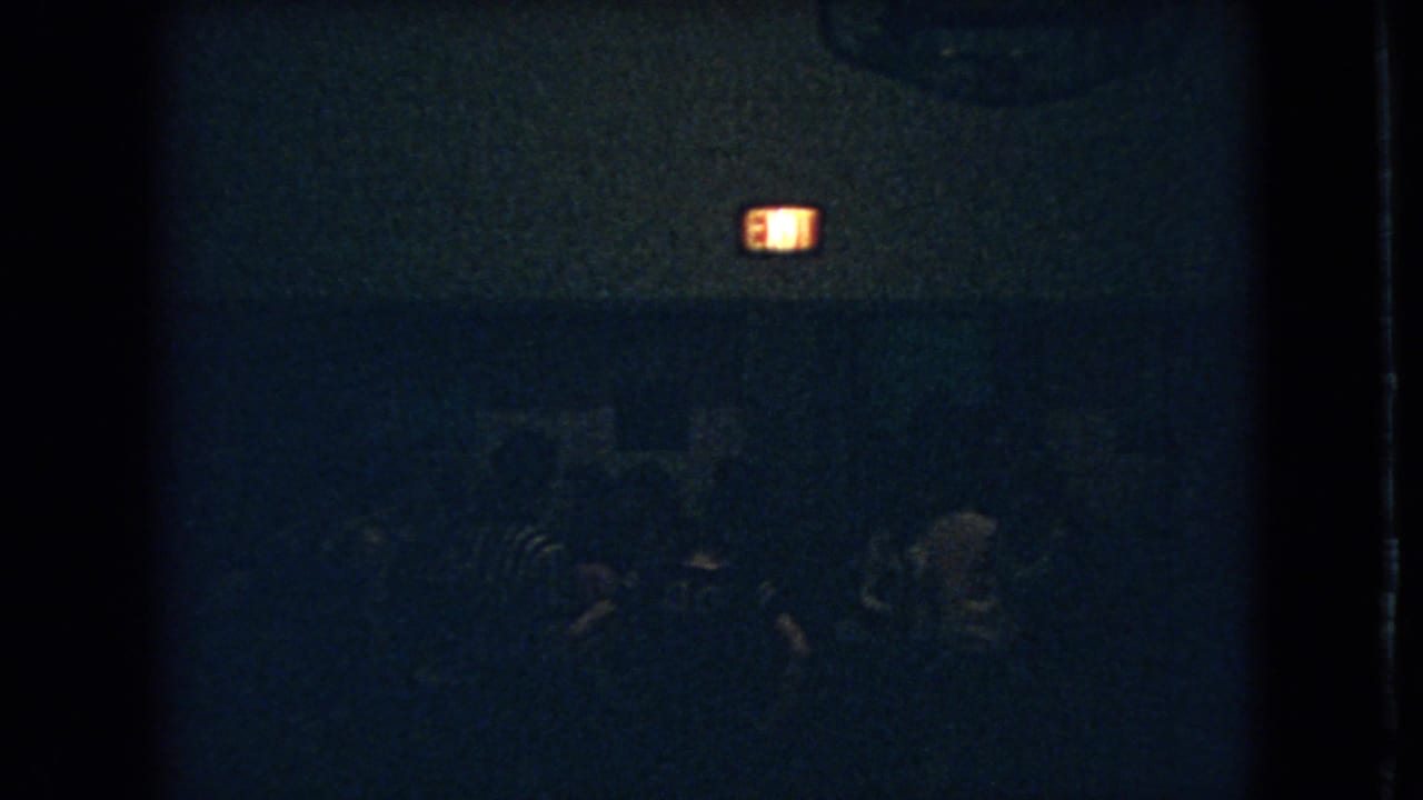 Silhouetted people in a dark room near an exit sign.