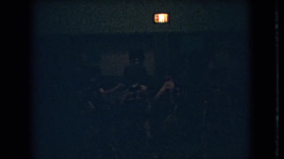 1966 Ohio 8mm frame with a glowing exit sign over faint silhouettes that appear to be players in a dark gymnasium.