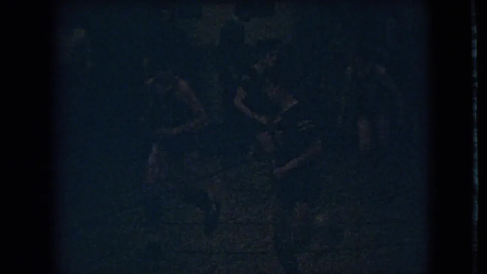1966 Ohio 8mm frame showing indistinct figures in a dark gymnasium, with movement suggested by blurred bodies and low exposure.