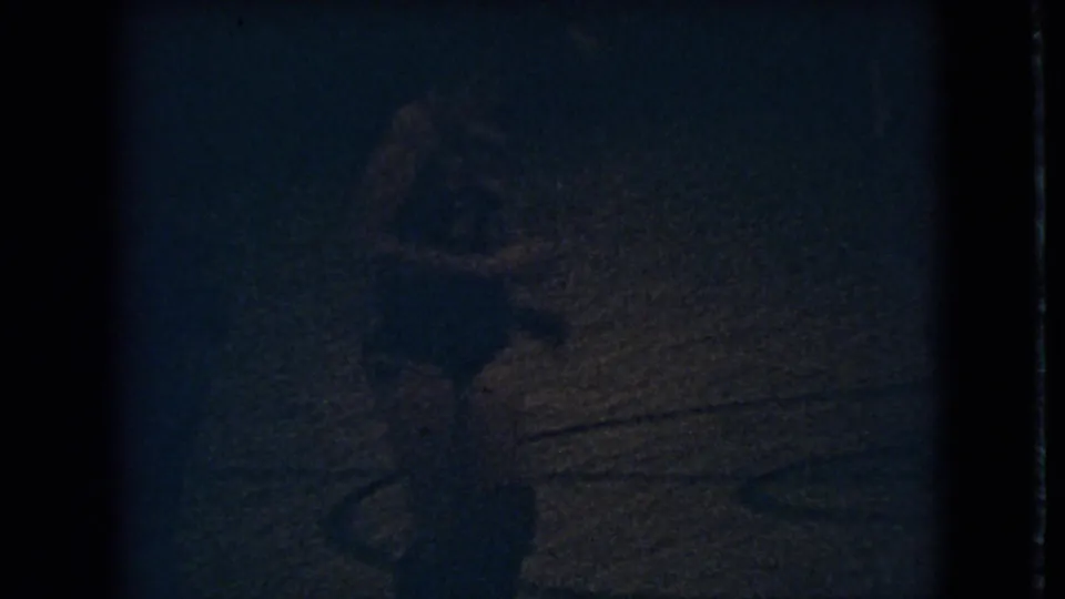 1966 Ohio 8mm frame showing a dark gym floor area with a faint human figure shape and pronounced low-light film grain.