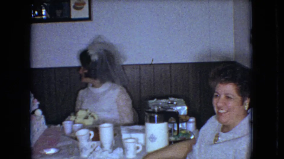 1966 Ohio 8mm frame showing a bride in profile and a smiling guest at a wedding reception table with cups, a coffee pot, and part of the cake visible.
