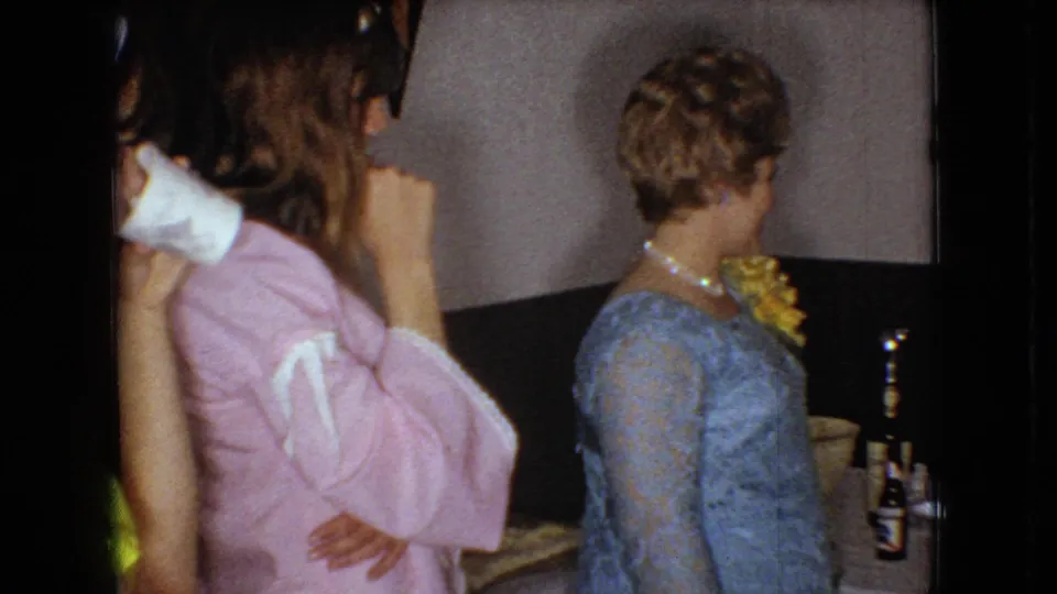 The final 1966 Ohio frame shows the woman in pink in the foreground and the woman in the blue lace dress turned toward the reception table, with a bottle, glasses, and the seated man partly visible.