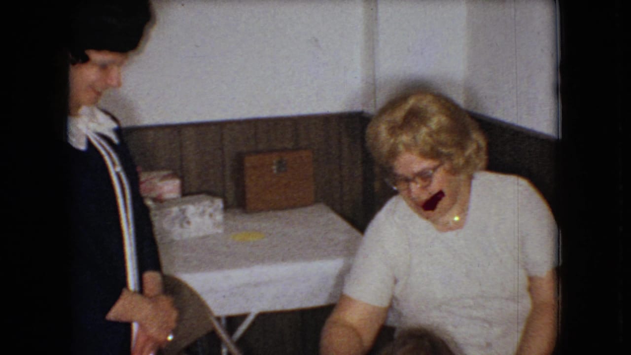 Standing woman watches as another woman in glasses laughs near a table.