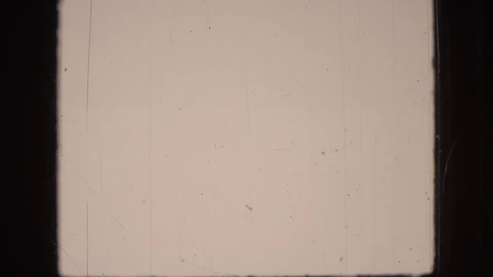 A pale, overexposed 8mm frame shows mostly blank pinkish film surface with fine scratches, dust, and dark frame edges.