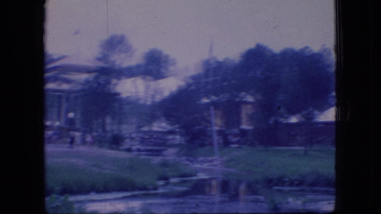 1966 Ohio 8mm frame showing white tents, a low pavilion-like structure, lawn, trees, and water viewed through a dark window or structural frame.