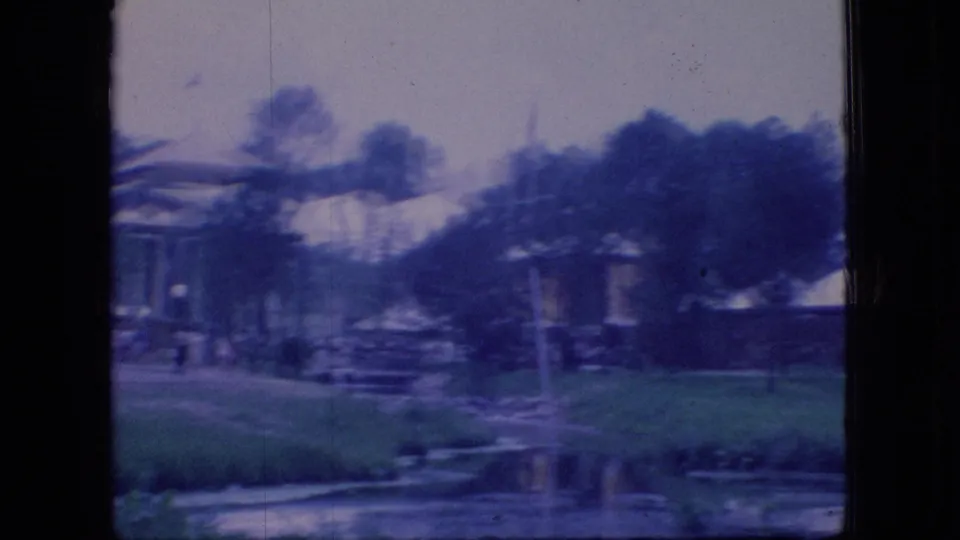 1966 Ohio 8mm frame showing white tents, a low pavilion-like structure, lawn, trees, and water viewed through a dark window or structural frame.
