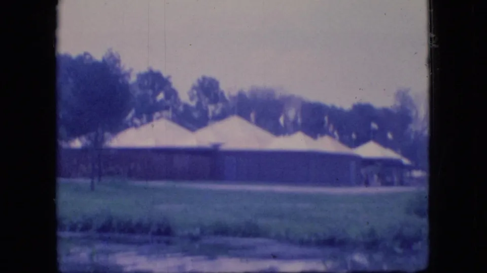 1966 Ohio 8mm still showing a row of white tents on open grass with trees in the background and soft blue film color.