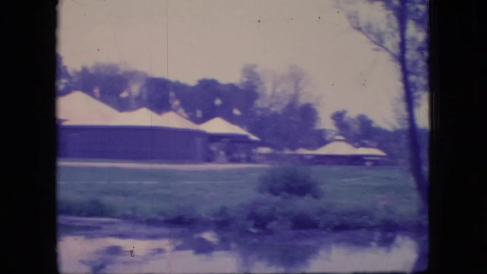 1966 Ohio lakeside park view with a pavilion or shelter building, light rooflines, lawn, shoreline brush, and reflected water in the foreground.