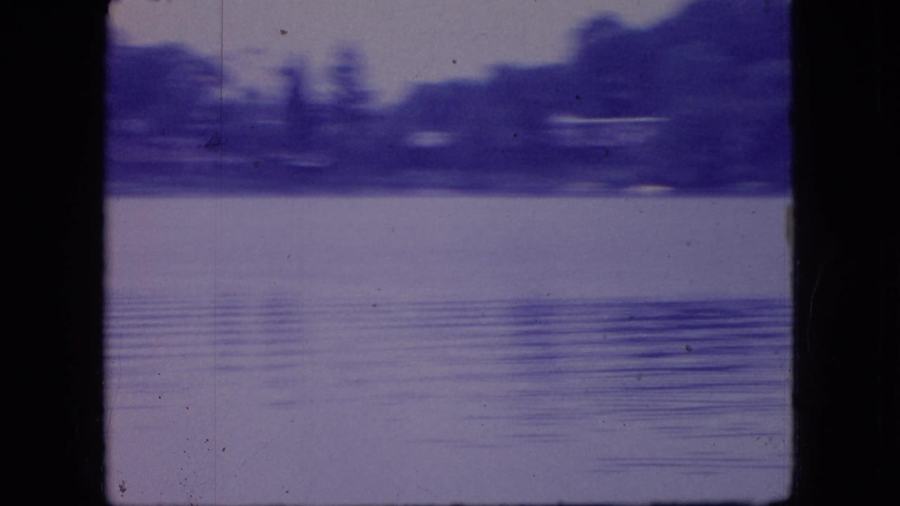 1966 Ohio 8mm frame looking across calm lake water toward a distant wooded shoreline, with soft focus, film grain, scratches, and black scan borders.