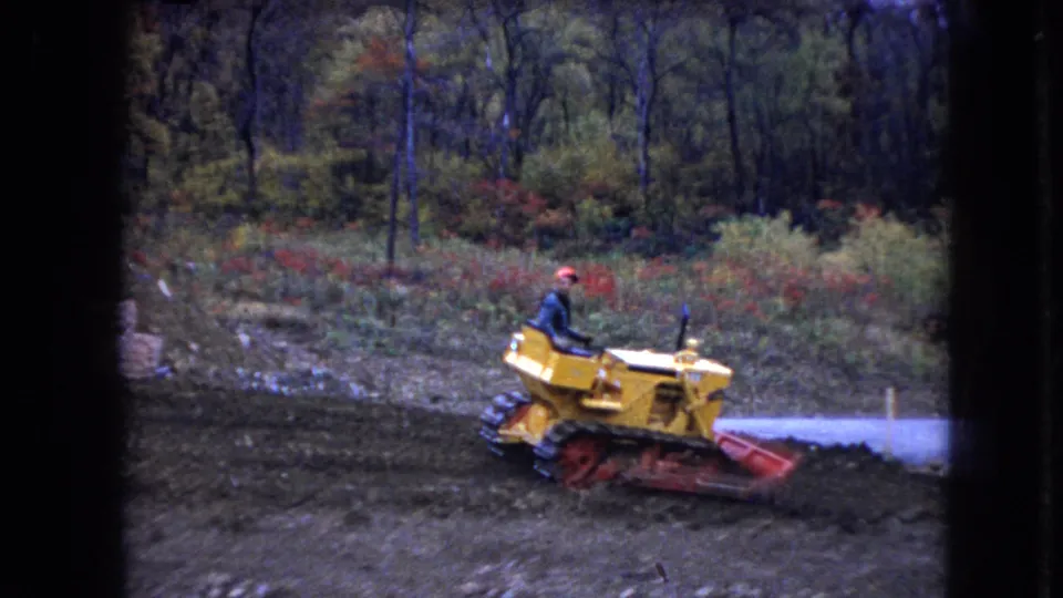 A man drives a yellow tracked bulldozer in the Ohio construction-site footage, with muddy earth in front and a pale road or path behind him.