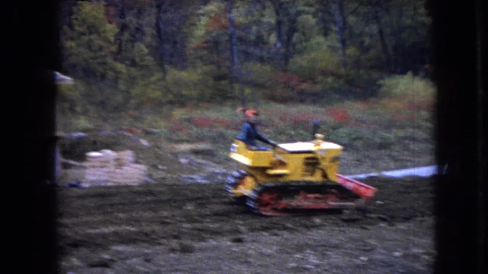 The yellow tracked bulldozer continues across a muddy Ohio work site, with stacked materials and trees visible in the background.