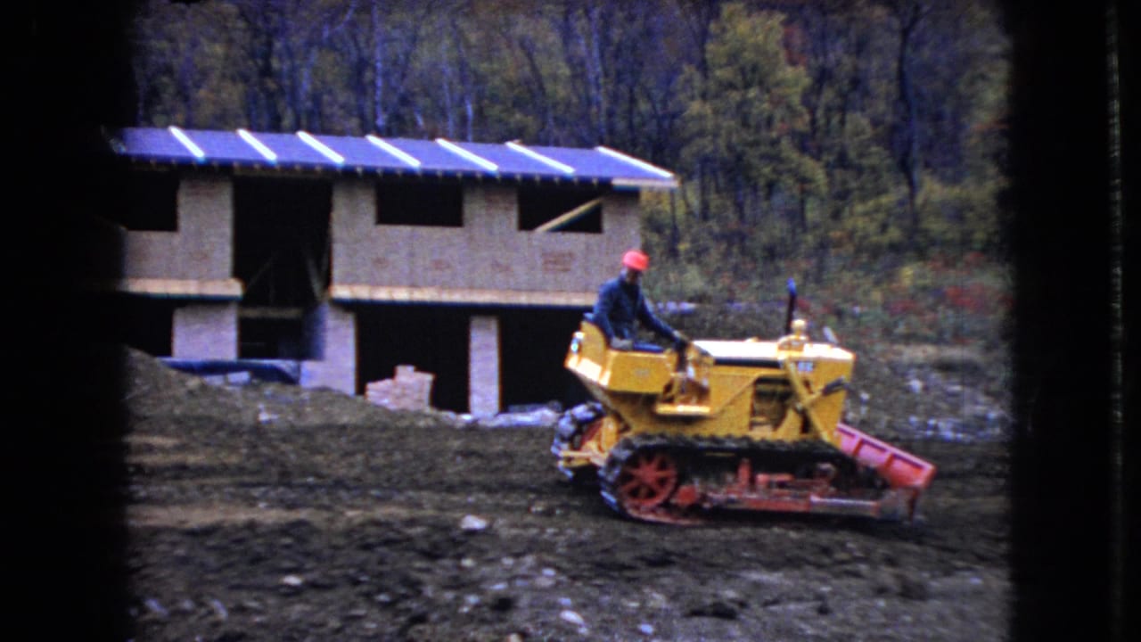 Yellow bulldozer moves past a partially built structure with stacked materials nearby.
