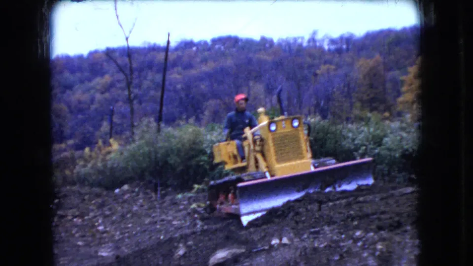 The bulldozer faces toward the camera with its front blade lowered on rough rural ground, continuing the 1966 Ohio home-movie view of construction work.
