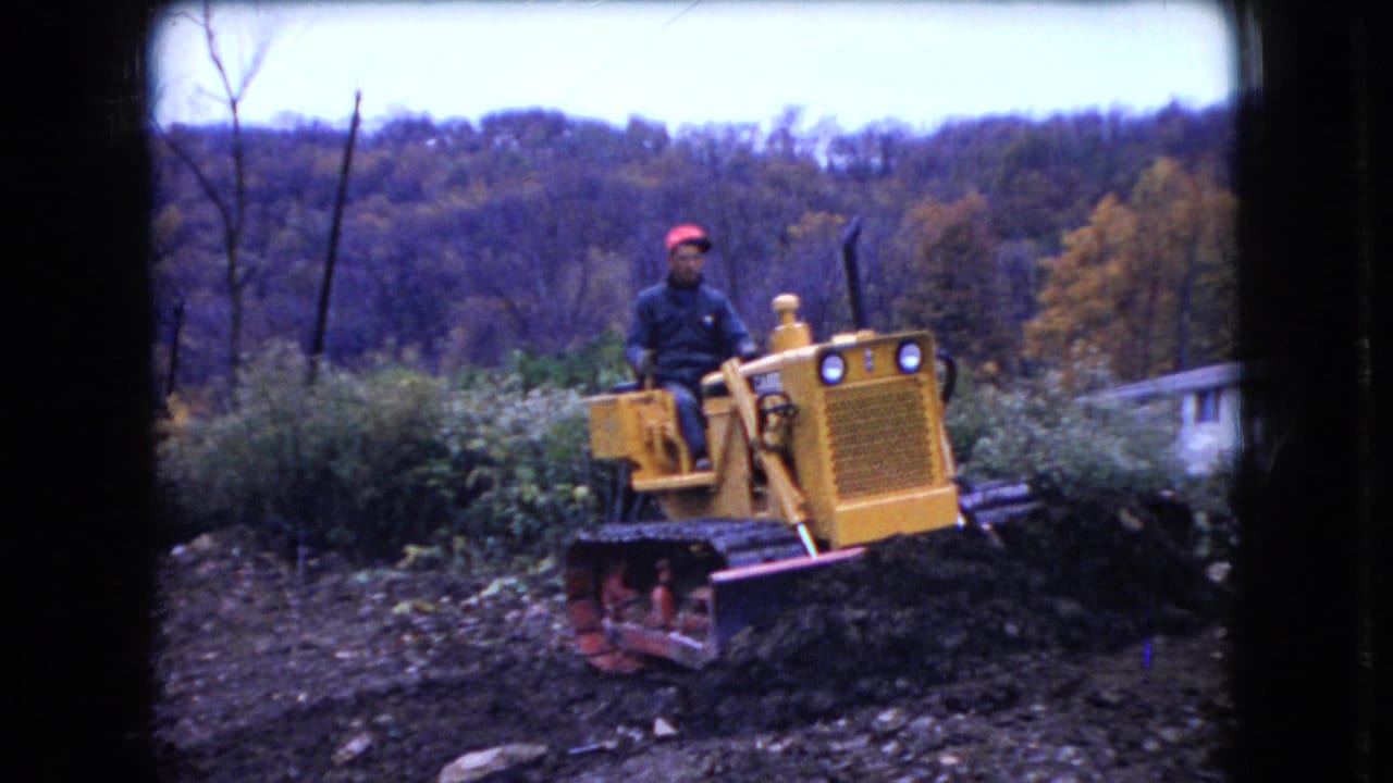 Yellow bulldozer climbs over dark earth while a man operates it outdoors.