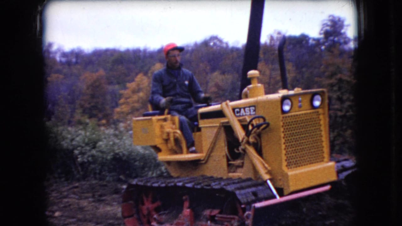 The operator sits upright on the yellow Case bulldozer as it passes through a wooded Ohio setting in the 1966 8mm footage.