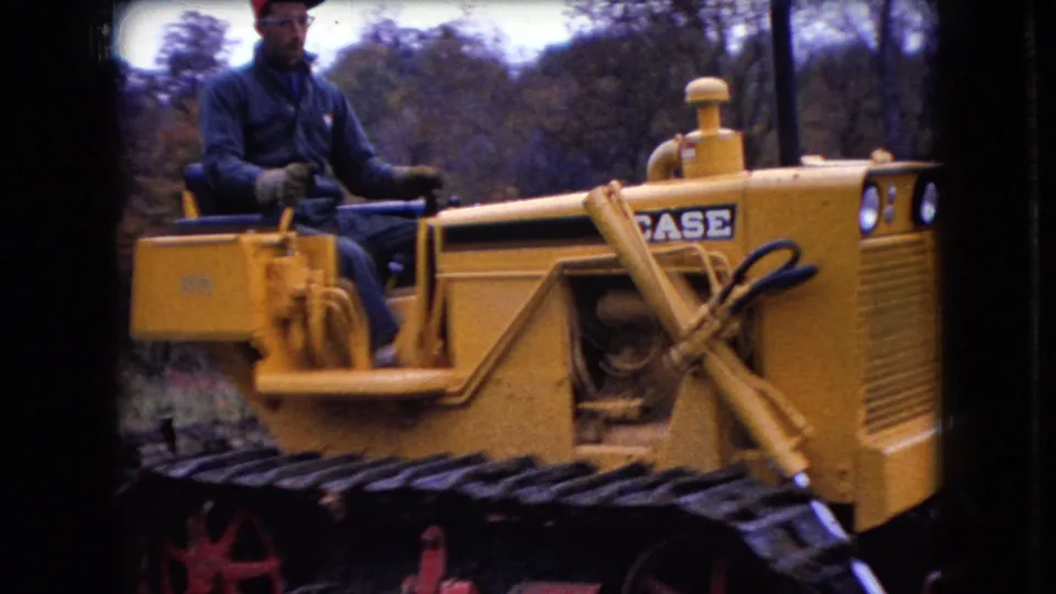 A closer frame shows the laborer seated at the controls of the yellow Case bulldozer, with the tracked base and wooded background visible.