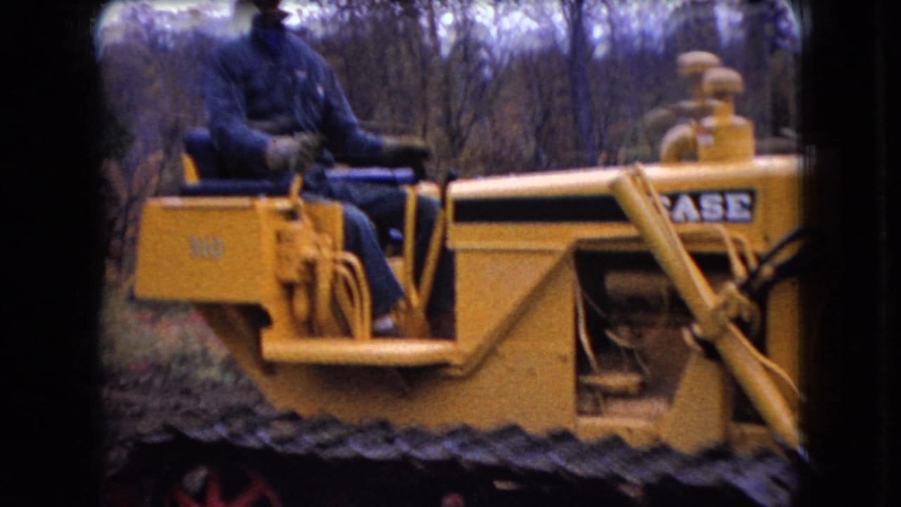 1966 Ohio 8mm frame showing a yellow Case 310 tracked bulldozer in a wooded area, with the seated operator partly cropped by the home-movie frame.