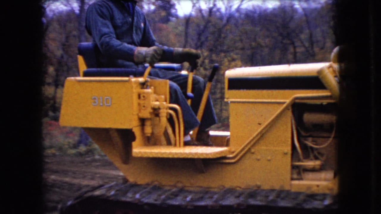 Side view from the 1966 Ohio home movie showing the Case 310 bulldozer body, controls, and operator against a wooded hillside.