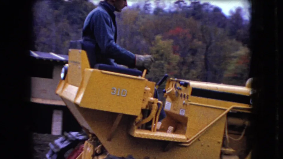 Final 1966 Ohio frame showing the yellow Case 310 bulldozer from the side, with its operator seated above the tracks and autumn-colored woods in the background.