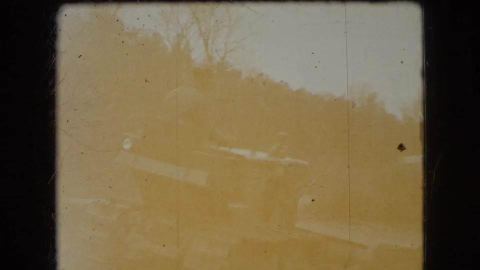 A heavily faded 8mm frame shows the yellow bulldozer and wooded hillside with low contrast and visible dust or film marks.