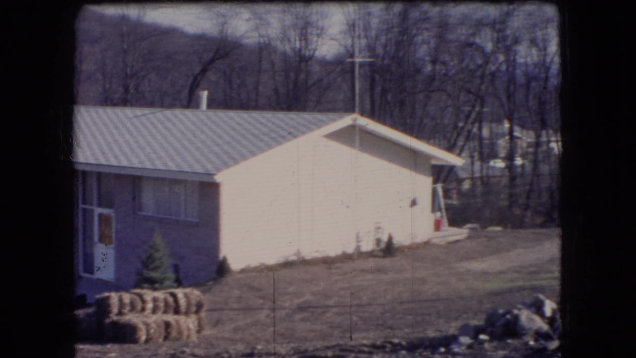 1966 Ohio rural roadside view of a modest light-colored house with a metal roof, stacked hay bales, a driveway, and leafless trees in the background.