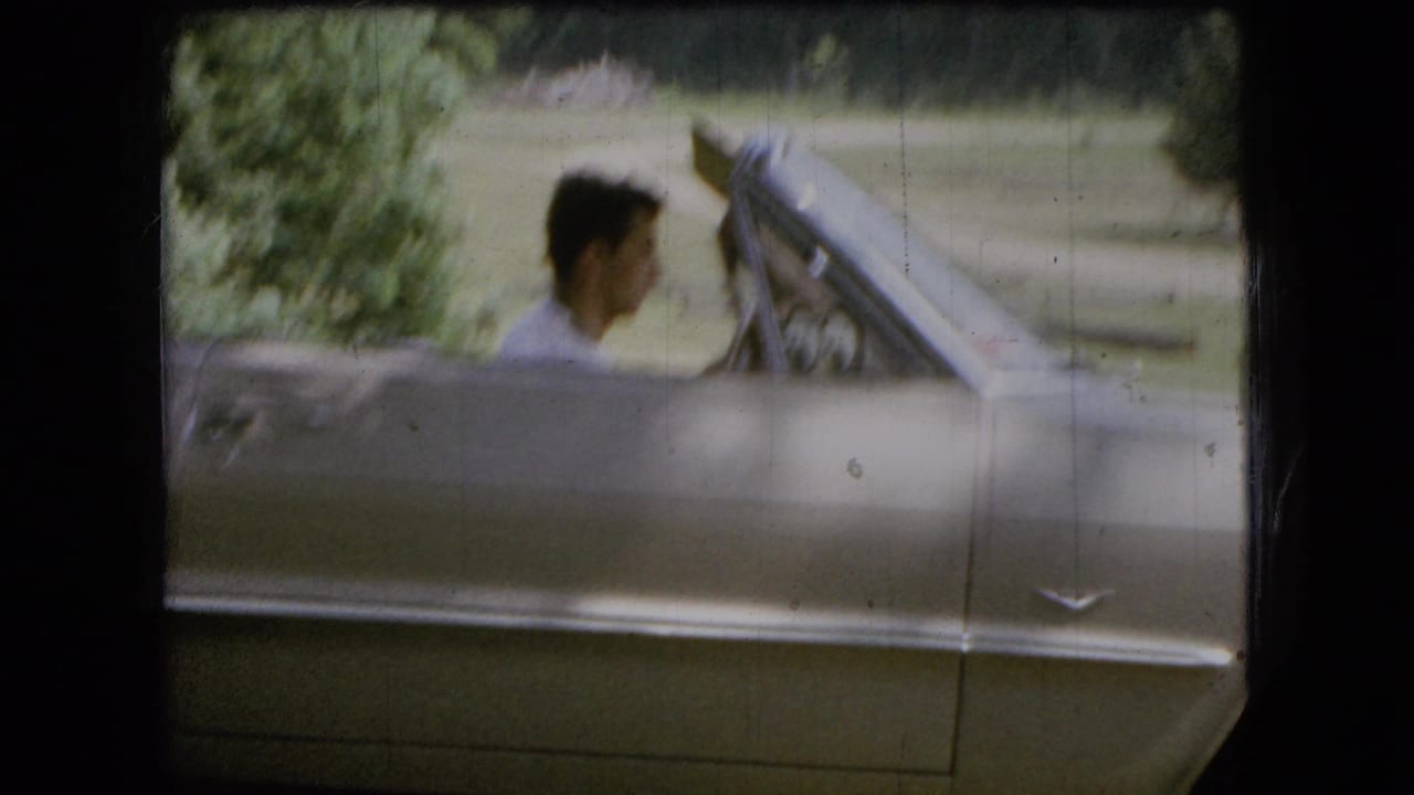 In 1966 Ohio home-movie footage, a young man in a light shirt sits in a silver convertible with the top down beside grass and trees.