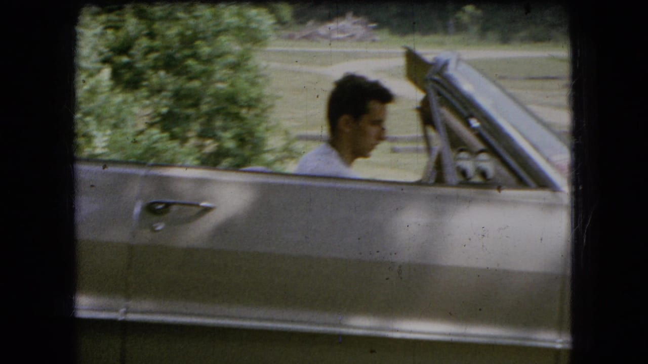 Side view of a young man in the driver's seat of a silver convertible outdoors.