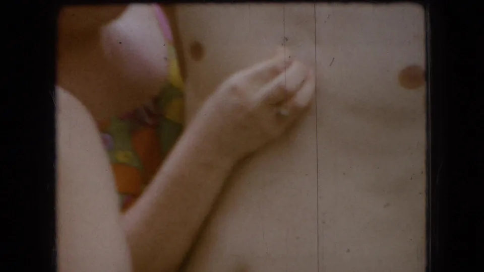 The woman appears to smile while using a ringed hand to touch or scratch the man's bare chest, with patterned swim fabric partly visible behind them.