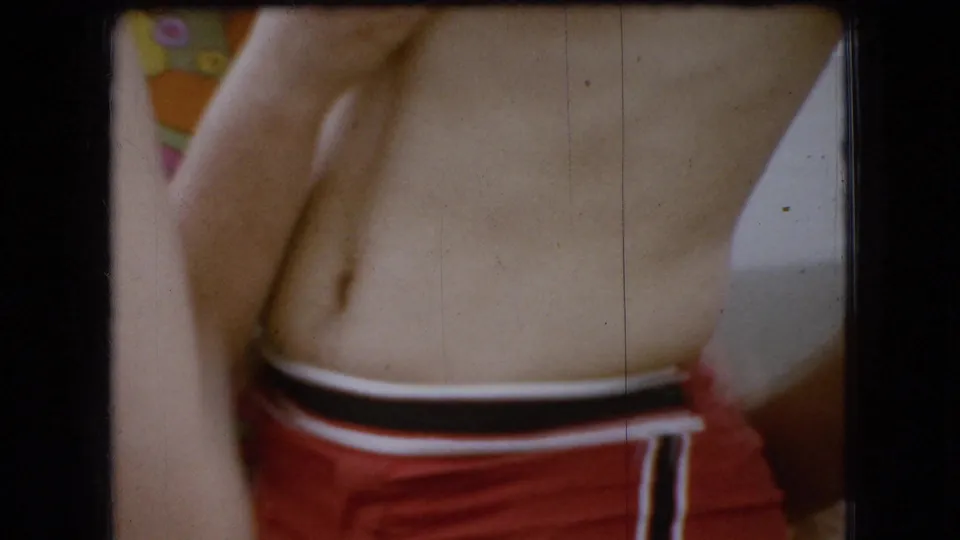 The final frame centers on the man's bare torso and red swim trunks, with the woman's shoulder and white swimsuit strap close at left in the tightly cropped 8mm composition.