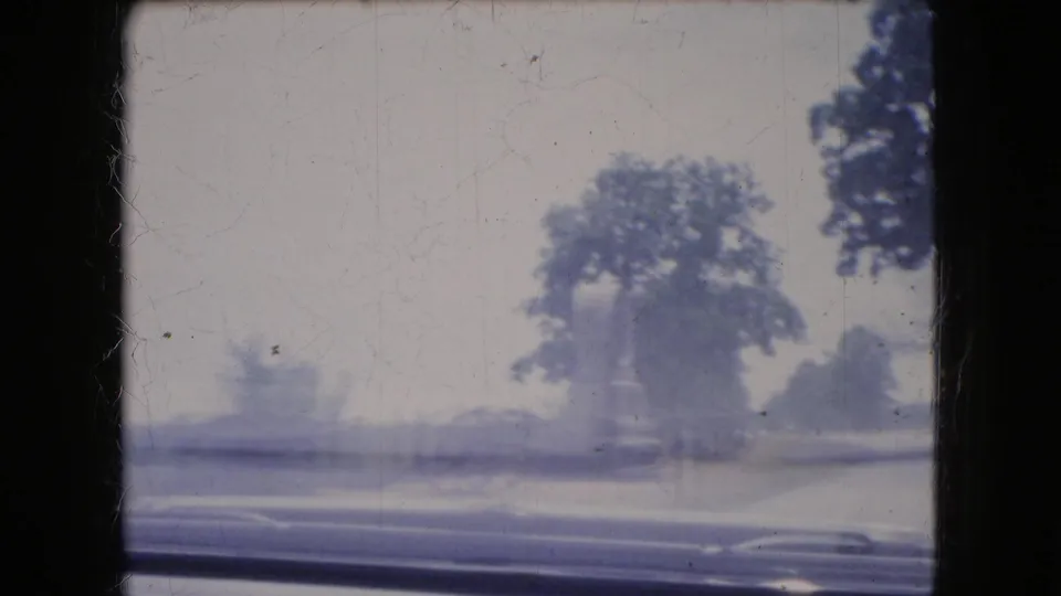 1966 Ohio 8mm frame showing a soft, blue-cast roadside view from a moving car, with trees, pavement, and a distant automobile passing through motion blur.