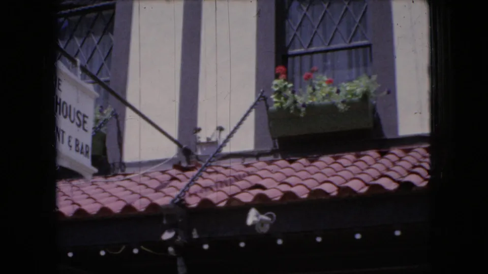 1966 Ohio home-movie frame showing a close passing view of a storefront-like facade with red roof tiles, upper windows, flower boxes, and a partially readable sign.