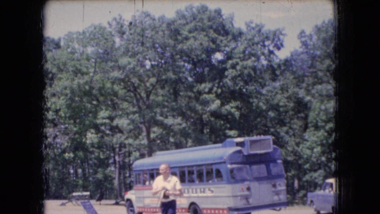 1966 Ohio 8mm frame showing a blue-and-white tour bus at a wooded stop, with a man holding a camera in the foreground and passengers visible through the windows.