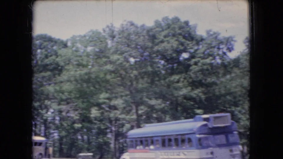 1966 Ohio 8mm frame showing the side and front of a blue-and-white tour bus against a wooded backdrop, with part of another vehicle entering from the left.
