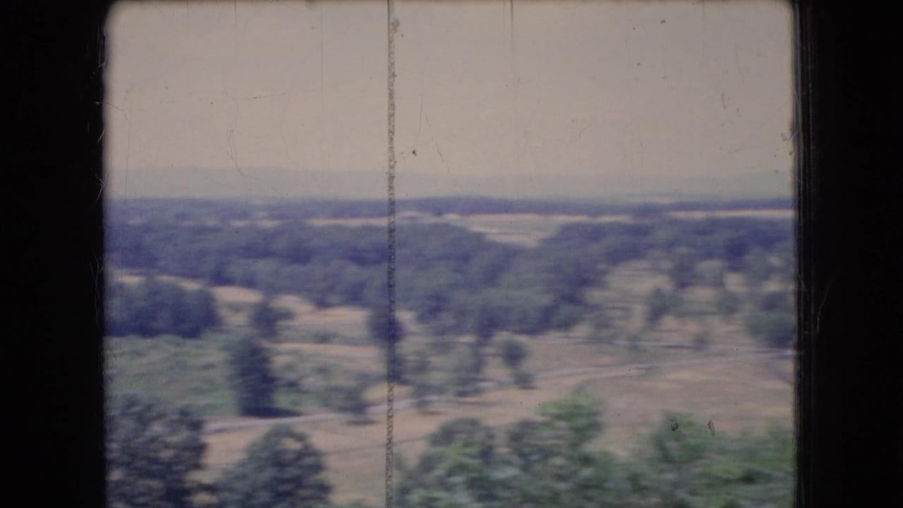 1966 Ohio 8mm view of a flat rural landscape with scattered trees, muted fields, a hazy sky, and a dark window or film-frame edge crossing the view.