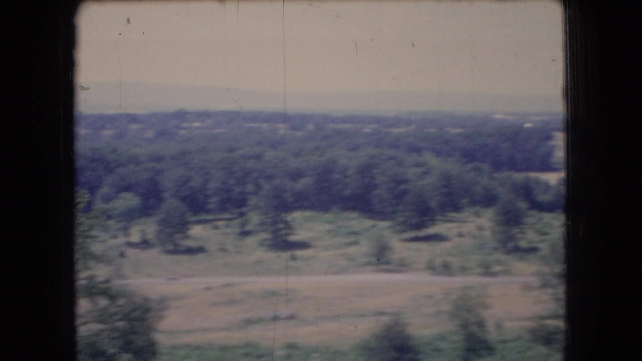 1966 Ohio home-movie frame showing wooded areas, open fields, and a distant flat horizon under a pale hazy sky.