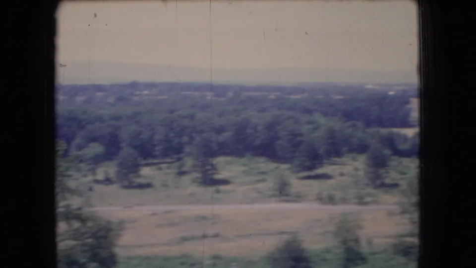 1966 Ohio home-movie frame showing wooded areas, open fields, and a distant flat horizon under a pale hazy sky.