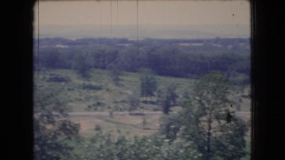 1966 Ohio 8mm frame of a soft-focus rural view with foreground trees, open ground, darker wooded areas, and a hazy distant horizon.