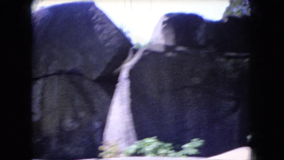 1966 Ohio home-movie frame showing large rock formations with a narrow stream or walkway-like passage between shadowed stone walls.